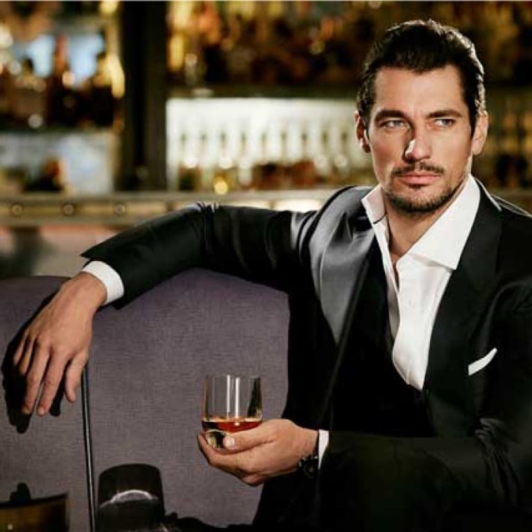 A man in a suit sits in a bar holding a glass of liquor.