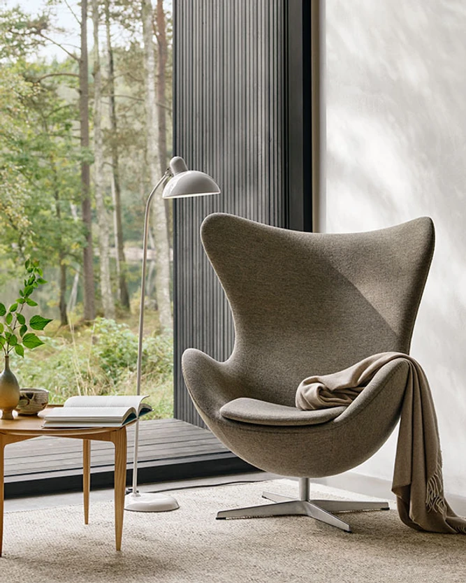 Modern chair with blanket in a serene room overlooking a forest.