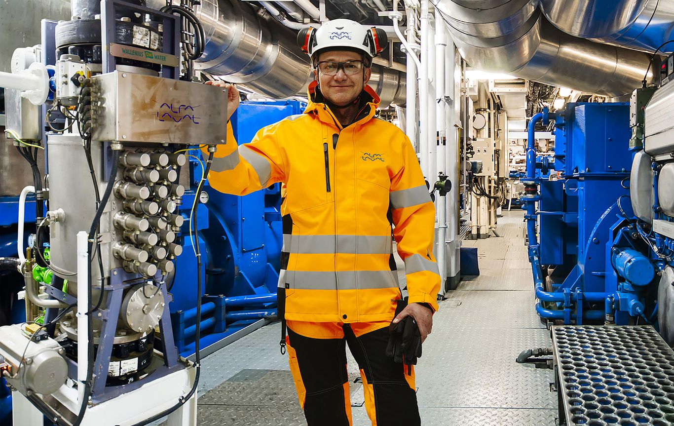 A worker in high-visibility clothing standing in an industrial facility with complex machinery.